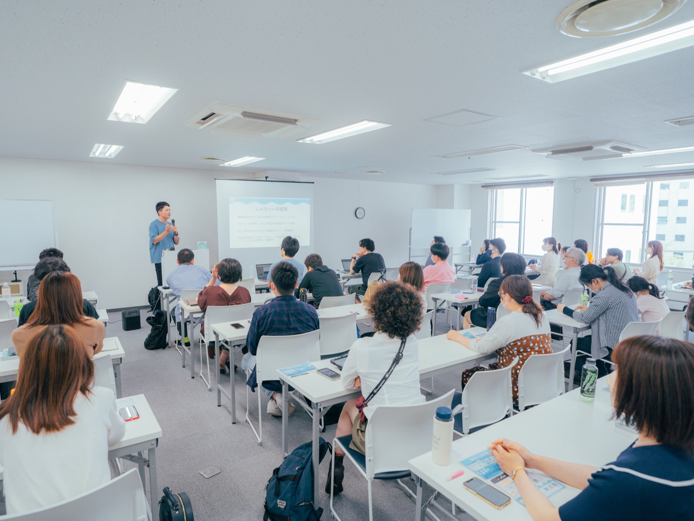 教室でマイクを持ち、自身の経歴を語りながら登壇するしゅうへい